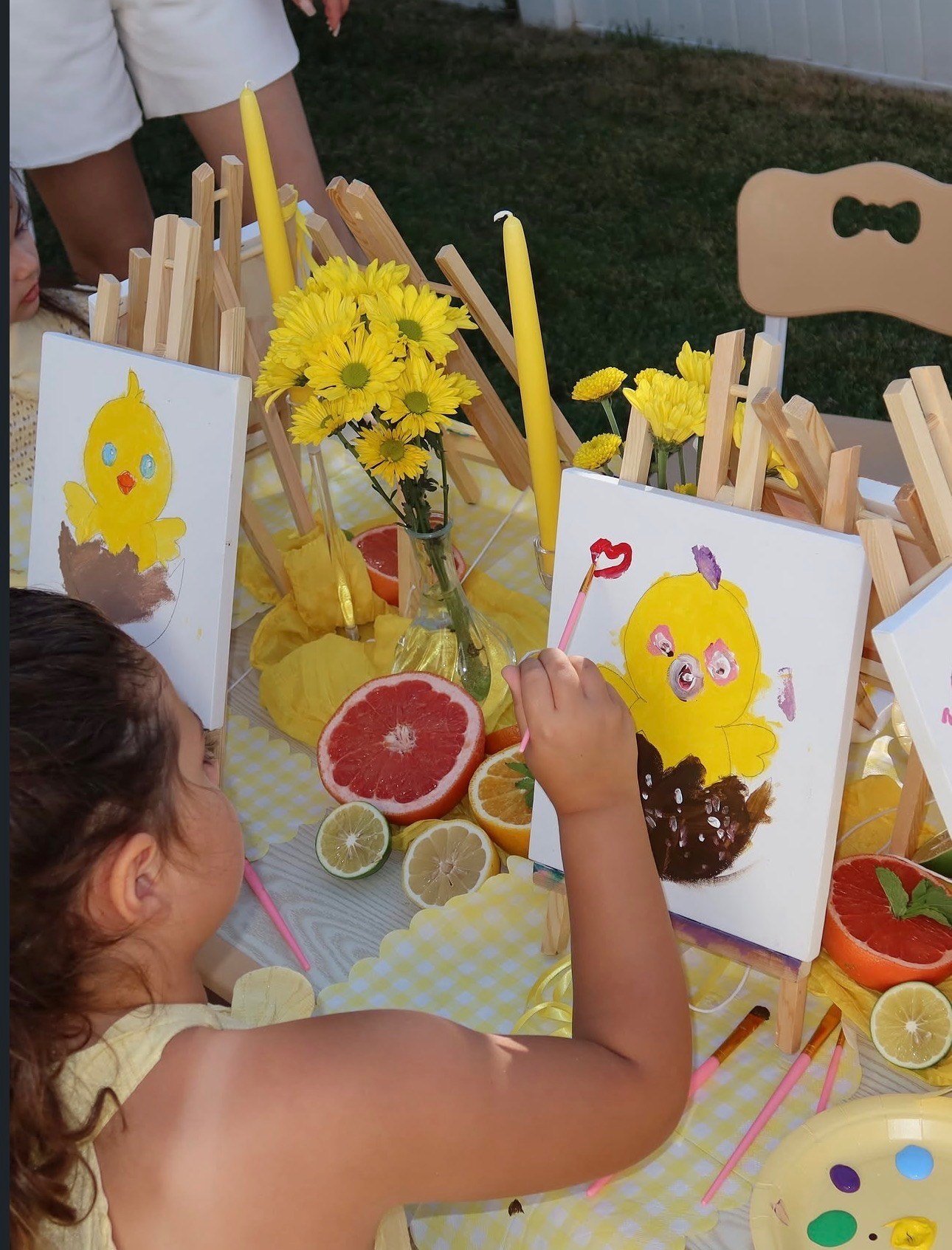 Child painting a yellow chick during an outdoor art activity at Top-Top Day Care