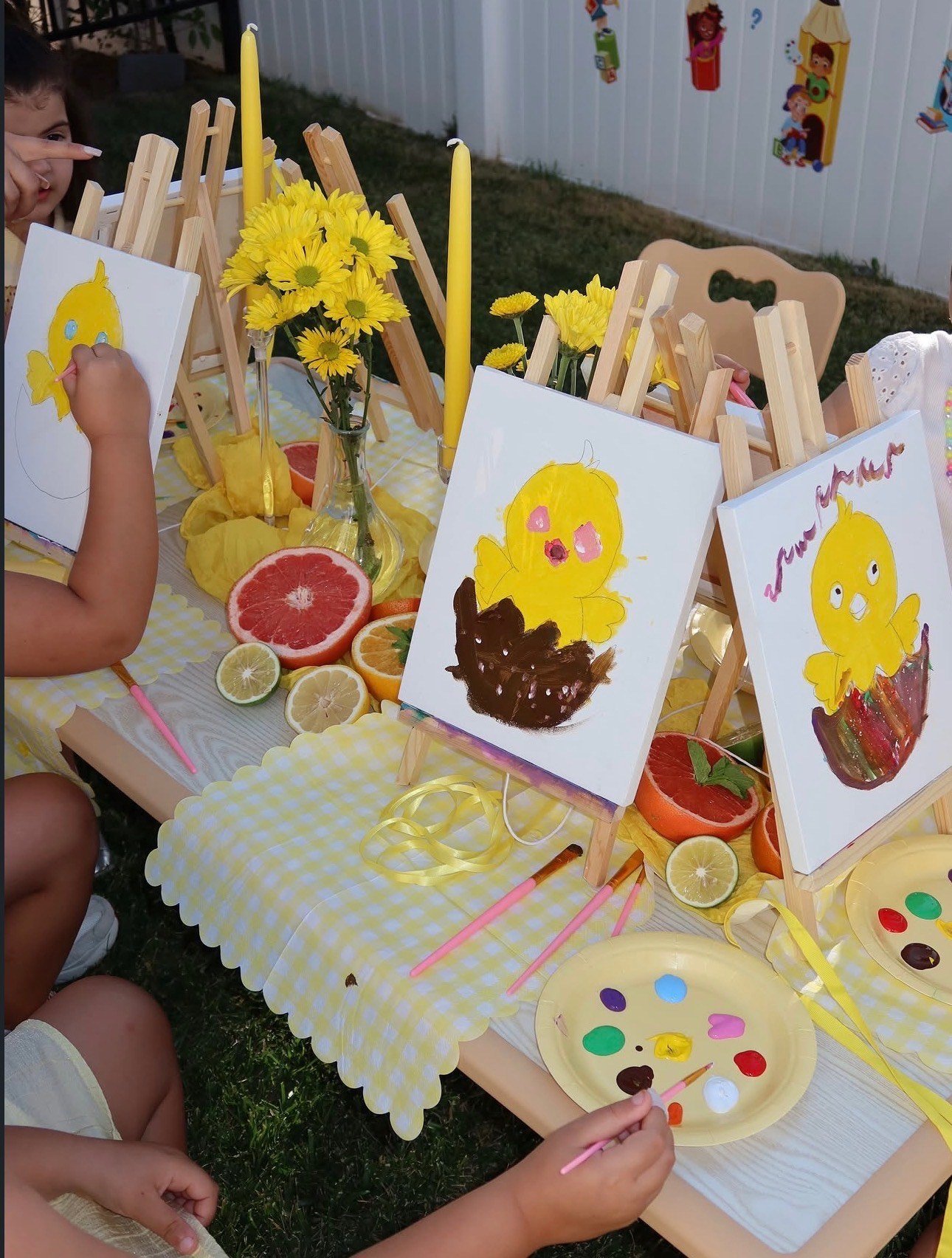 Children painting yellow chick pictures at outdoor easels